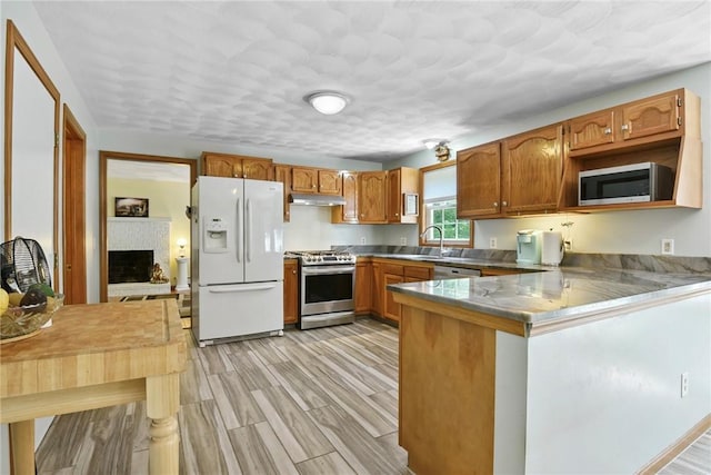 6 Ferris Dr, Coventry, RI 02816 - kitchen with appliances with stainless steel finishes, a peninsula, brown cabinetry, a fireplace, and under cabinet range hood