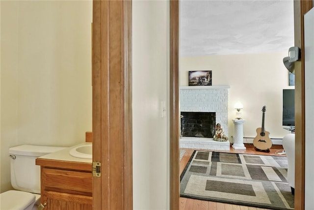 6 Ferris Dr, Coventry, RI 02816 - half bath featuring vanity, a brick fireplace, a baseboard radiator, and wood finished floors