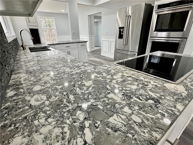 20 Biscuit Hill Rd, Foster, RI 02825 - kitchen featuring appliances with stainless steel finishes, range hood, stone countertops, wainscoting, and white cabinetry
