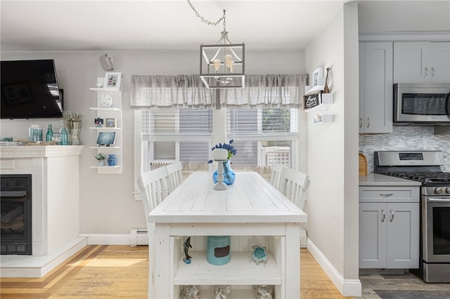 13 Vaughan Ave, Newport, RI 02840 - dining room featuring light wood finished floors, a chandelier, a baseboard heating unit, and a glass covered fireplace