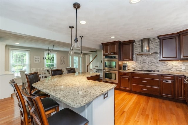 11 Greenbrier Rd, Smithfield, RI 02828 - kitchen featuring stainless steel appliances, wall chimney range hood, a breakfast bar area, light wood finished floors, and a kitchen island