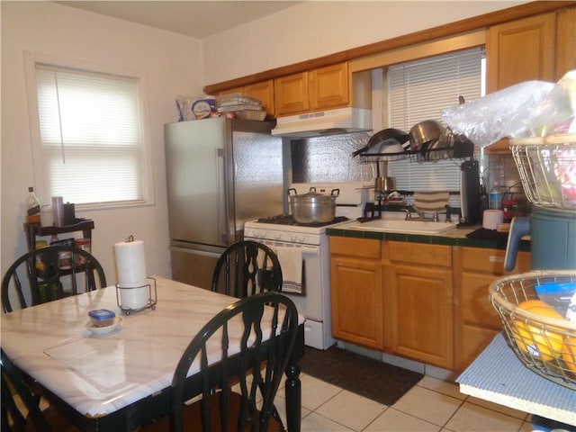 269 Althea St, Providence, RI 02907 - kitchen with under cabinet range hood, white range with gas cooktop, tile countertops, freestanding refrigerator, and light tile patterned floors