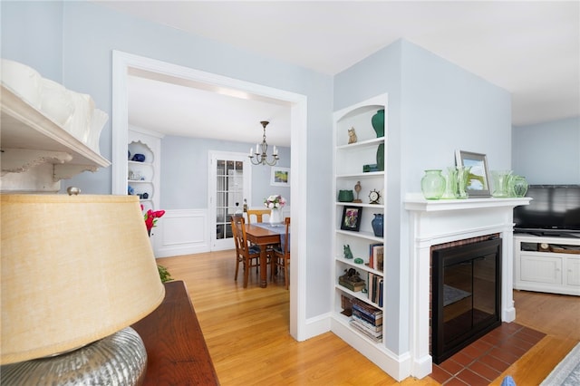 221 Trinity St, Warwick, RI 02886 - living area featuring light wood finished floors, a chandelier, built in shelves, a brick fireplace, and a wainscoted wall