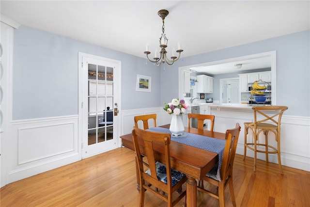 221 Trinity St, Warwick, RI 02886 - dining area with light wood-type flooring, a chandelier, wainscoting, and a decorative wall