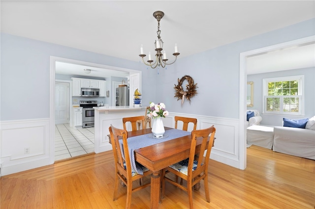 221 Trinity St, Warwick, RI 02886 - dining area featuring a chandelier, a wainscoted wall, light wood-style floors, and a decorative wall