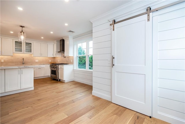 5 Williams St Unit 4, Warwick, RI 02818 - kitchen with high end stove, a barn door, wall chimney range hood, light wood finished floors, and white cabinetry