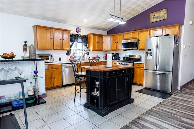 61 Cyr St, Providence, RI 02905 - kitchen featuring appliances with stainless steel finishes, vaulted ceiling, decorative backsplash, a kitchen island, and light tile patterned floors