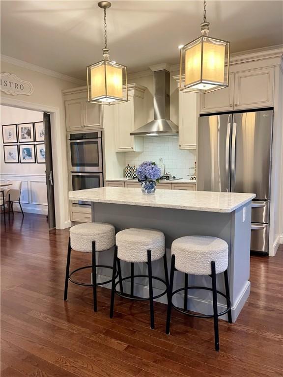21 Helm St, Jamestown, RI 02835 - kitchen featuring wall chimney exhaust hood, appliances with stainless steel finishes, ornamental molding, a breakfast bar, and a kitchen island