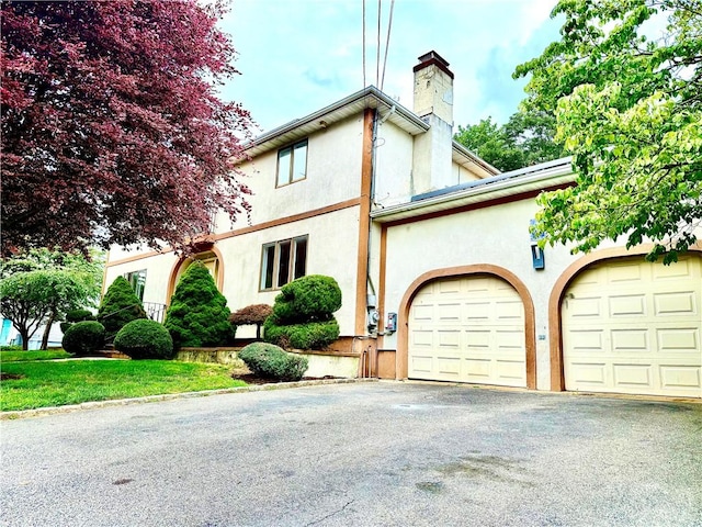 74 Plymouth Rd, East Providence, RI 02914 - view of front of property with a garage, asphalt driveway, a chimney, and stucco siding