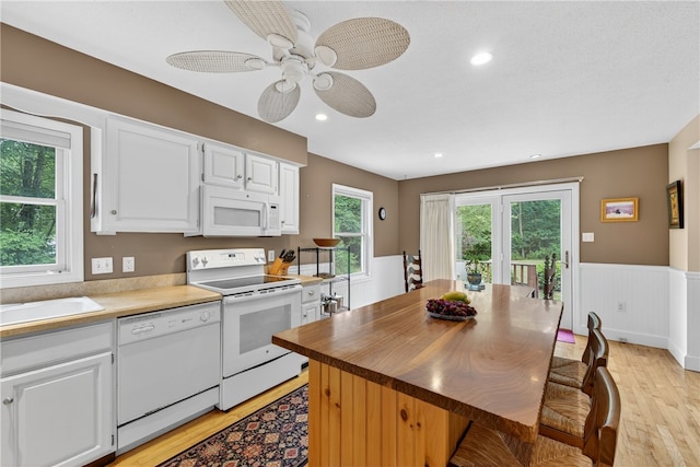 435 Allen Ave, South Kingstown, RI 02879 - kitchen with white appliances, light wood-style flooring, white cabinets, a wainscoted wall, and a ceiling fan
