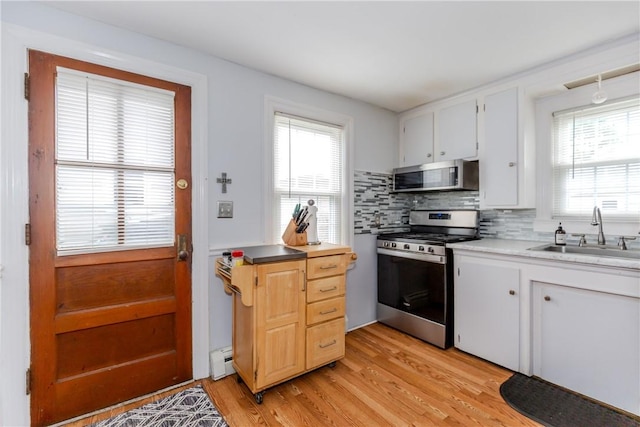 36 Walton St, Providence, RI 02908 - kitchen with stainless steel appliances, baseboard heating, tasteful backsplash, light wood-style floors, and light countertops