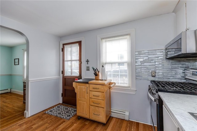 36 Walton St, Providence, RI 02908 - kitchen featuring stainless steel appliances, baseboard heating, arched walkways, decorative backsplash, and light wood-style flooring