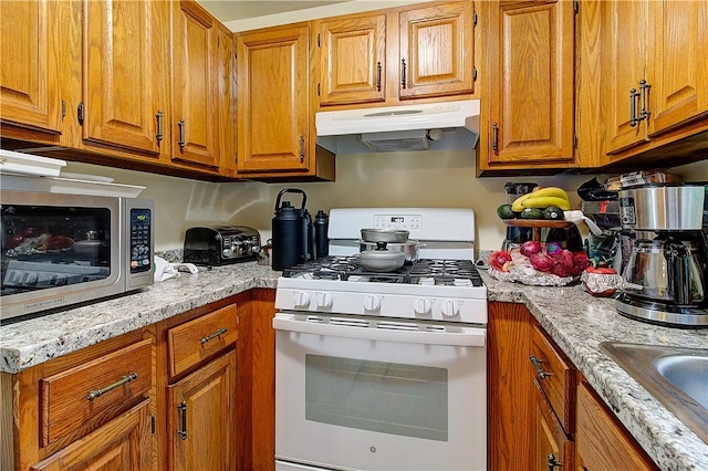 10 E St Unit 316, Cranston, RI 02920 - kitchen with white gas range, under cabinet range hood, brown cabinetry, and stainless steel microwave