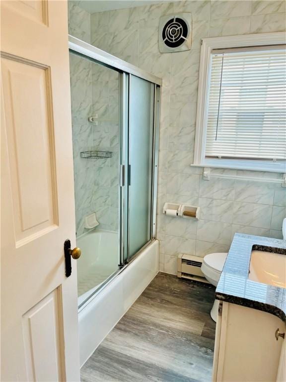 74 Leslie St, Cranston, RI 02910 - bathroom featuring vanity, bath / shower combo with glass door, a baseboard radiator, tile walls, and wood finished floors