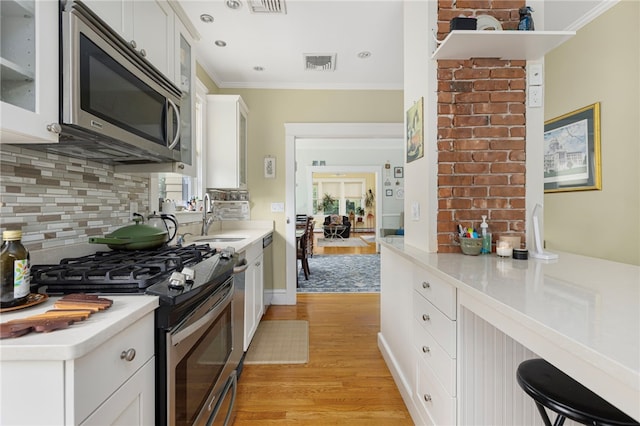 179 Cole Ave Unit 2, Providence, RI 02906 - kitchen featuring appliances with stainless steel finishes, crown molding, light wood-style floors, glass insert cabinets, and tasteful backsplash