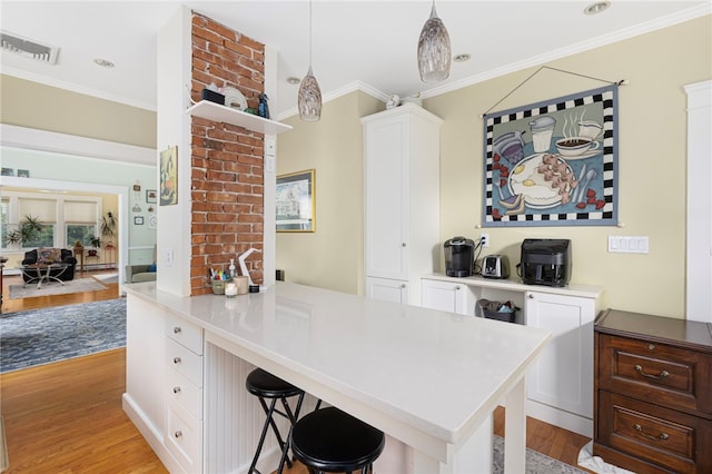179 Cole Ave Unit 2, Providence, RI 02906 - kitchen with light wood-style floors, ornamental molding, white cabinets, a kitchen breakfast bar, and hanging light fixtures