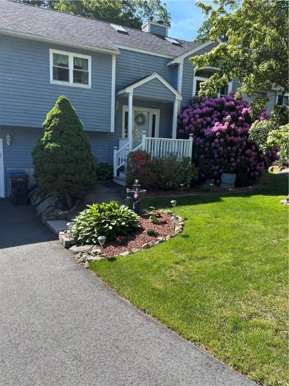 9 Ivy Hollow Ct, Cranston, RI 02921 - view of front facade featuring a front lawn, roof with shingles, a chimney, covered porch, and driveway