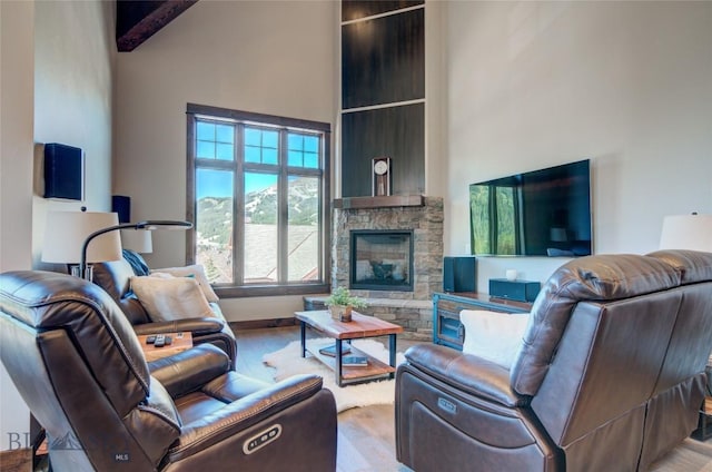 living room featuring beam ceiling, a stone fireplace, a towering ceiling, and light wood-type flooring