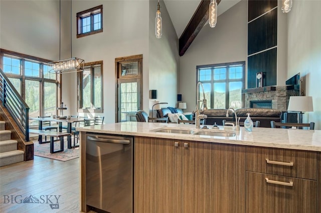 kitchen featuring dishwasher, sink, a high ceiling, a stone fireplace, and light stone counters