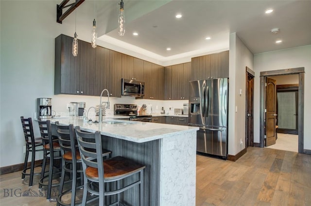 kitchen featuring a breakfast bar area, kitchen peninsula, light stone countertops, and appliances with stainless steel finishes