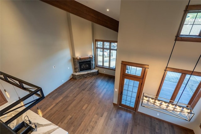 unfurnished living room featuring a stone fireplace, beamed ceiling, a high ceiling, and dark hardwood / wood-style floors