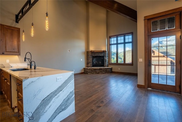 kitchen featuring a stone fireplace, sink, hanging light fixtures, beam ceiling, and light stone counters