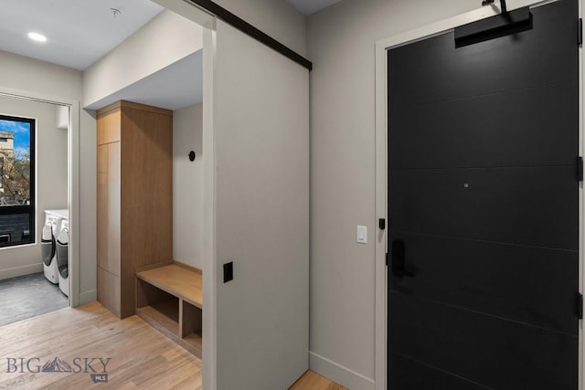 mudroom featuring light wood finished floors, a barn door, baseboards, and washer and clothes dryer