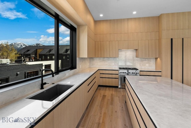 kitchen with tasteful backsplash, high end range, light wood-style floors, light brown cabinets, and a sink