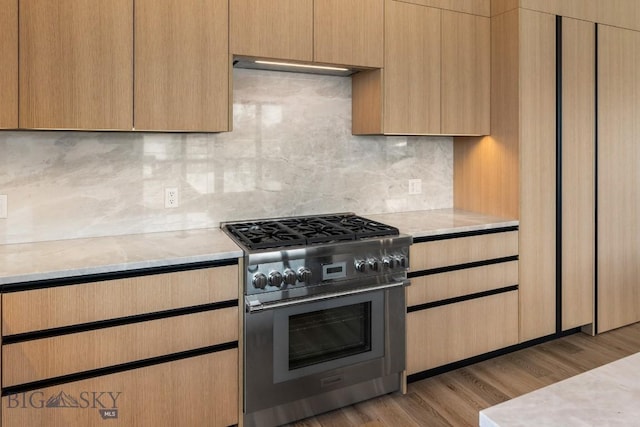 kitchen featuring stainless steel range, decorative backsplash, light brown cabinetry, light wood-style floors, and light stone countertops