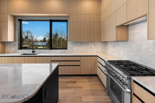 kitchen with light wood-style flooring, modern cabinets, high end stove, light brown cabinets, and a sink