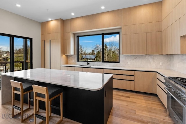 kitchen with stainless steel range, light wood-style flooring, light brown cabinets, a kitchen island, and modern cabinets