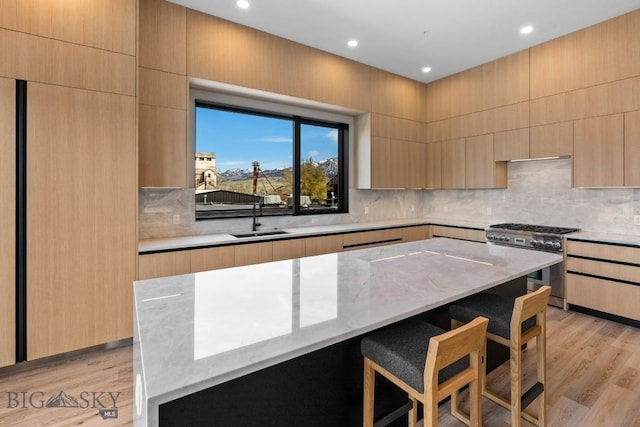 kitchen featuring light brown cabinets, a sink, gas range, light wood-type flooring, and a kitchen bar