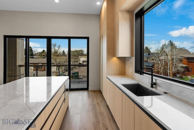 kitchen with light wood-style flooring, modern cabinets, light stone countertops, light brown cabinets, and a sink