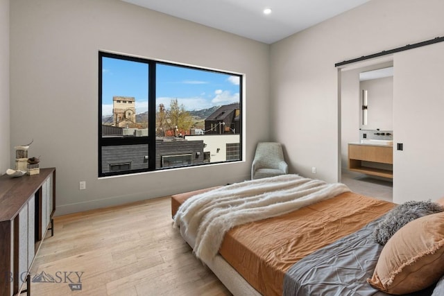 bedroom with recessed lighting, light wood-style flooring, a barn door, connected bathroom, and baseboards