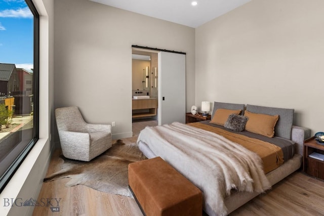 bedroom with a barn door, ensuite bath, and wood finished floors