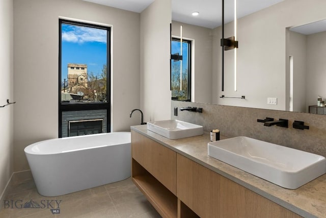 full bath featuring double vanity, a soaking tub, a sink, and a glass covered fireplace