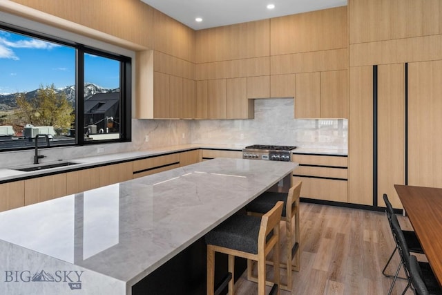 kitchen with modern cabinets, light wood-style flooring, light brown cabinetry, a sink, and light stone countertops