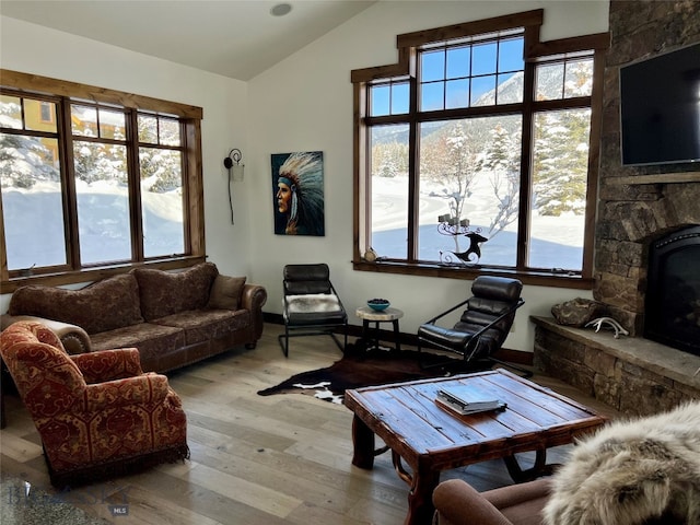 living room featuring lofted ceiling, a stone fireplace, and light wood-type flooring