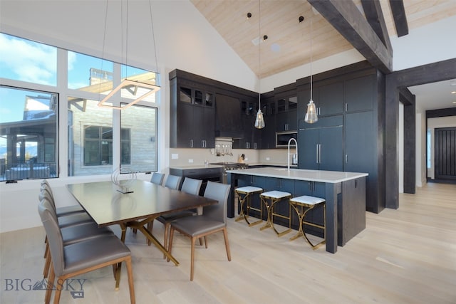 kitchen featuring hanging light fixtures, high vaulted ceiling, an island with sink, a breakfast bar area, and light wood-type flooring