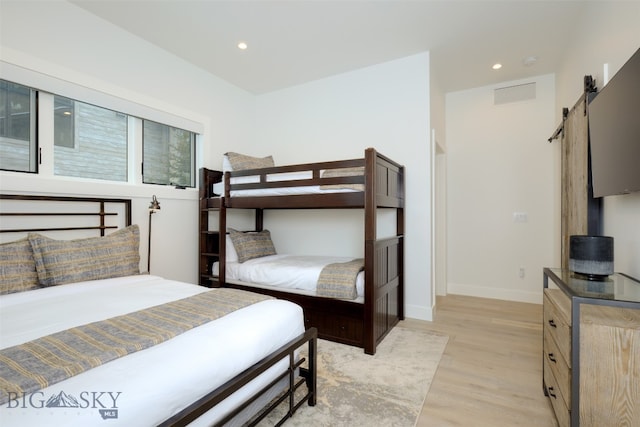 bedroom with a barn door and light hardwood / wood-style flooring