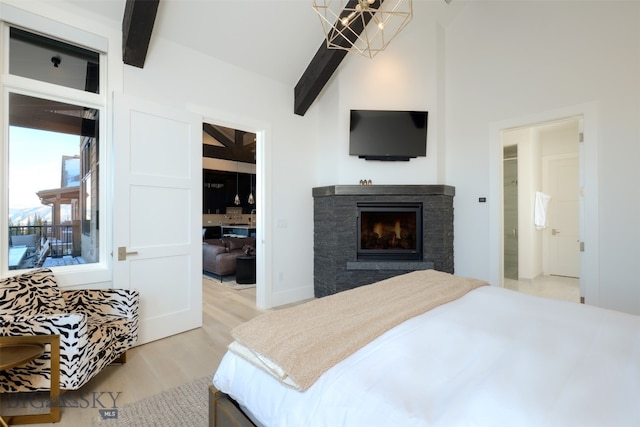 bedroom featuring beam ceiling, ensuite bath, hardwood / wood-style floors, a chandelier, and a fireplace