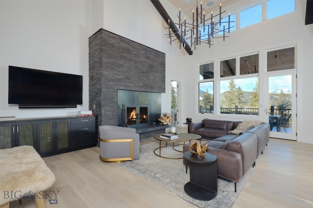 living room featuring light wood-type flooring, a towering ceiling, a fireplace, and a chandelier