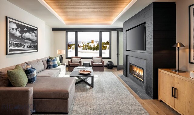 living room with wood ceiling, a fireplace, a tray ceiling, and light wood-style flooring