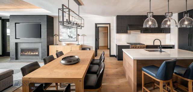 kitchen with light countertops, open floor plan, a sink, wall chimney range hood, and an island with sink