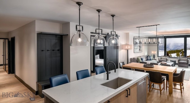 kitchen featuring a kitchen island with sink, a sink, open floor plan, dishwasher, and pendant lighting