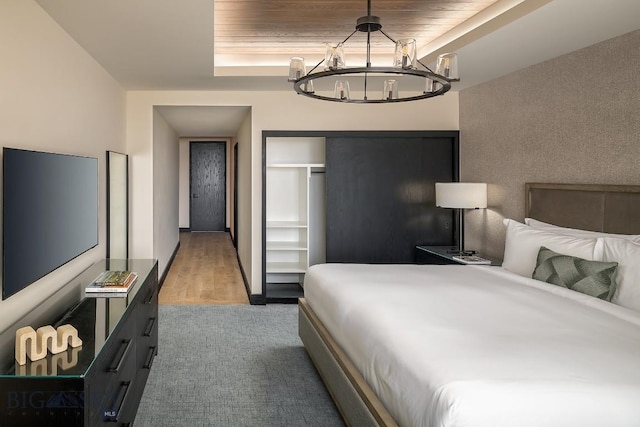 carpeted bedroom with wooden ceiling, a tray ceiling, a chandelier, and a closet