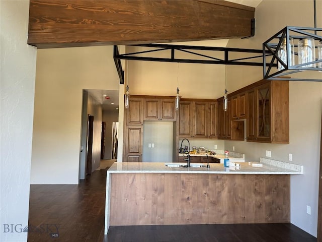 kitchen with dark wood-type flooring, a towering ceiling, kitchen peninsula, and sink