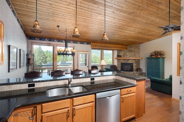 kitchen featuring dishwasher, decorative light fixtures, ceiling fan with notable chandelier, a stone fireplace, and light wood-type flooring