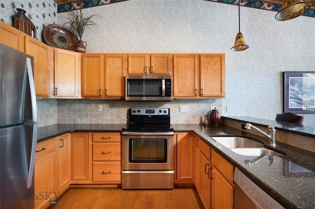 kitchen featuring appliances with stainless steel finishes, hanging light fixtures, dark stone counters, and light wood-type flooring