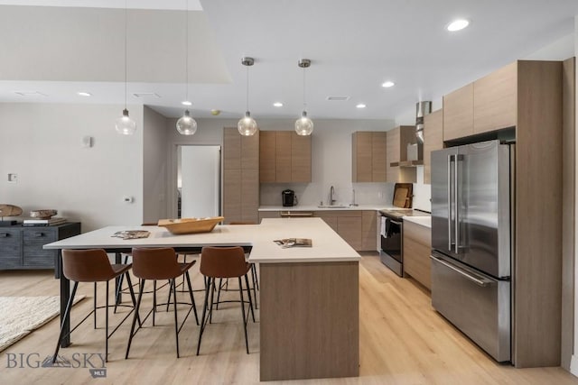 kitchen with appliances with stainless steel finishes, light wood-type flooring, a spacious island, pendant lighting, and a breakfast bar area